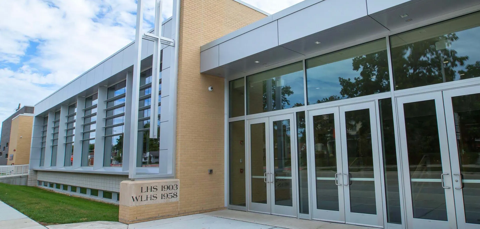 Il moderno edificio della Wisconsin Lutheran High School con facciata in vetro e mattoni è circondato da un'area verde e alberi.