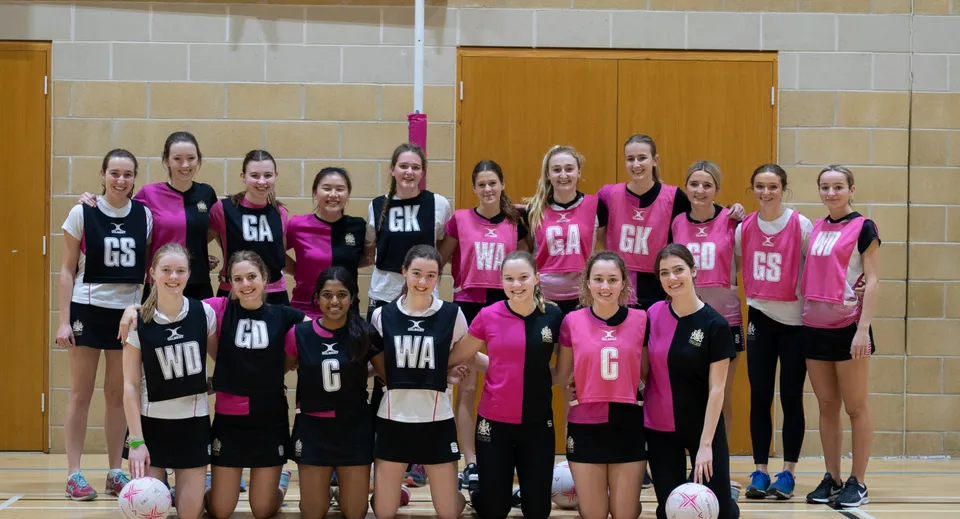 Un gruppo di giovani giocatrici di netball del Cheltenham College posa nella palestra con pavimento e pareti in legno.