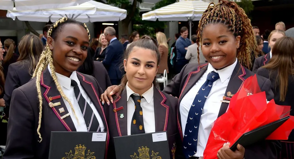 Tre studenti della Haileybury School sorridono insieme all'aperto all'interno del campus scolastico.