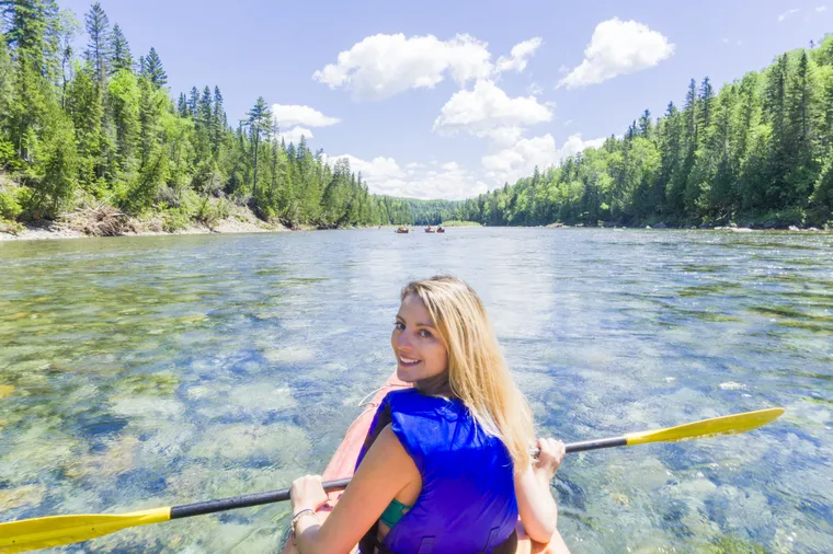 Lächelnde junge Frau mit Schwimmweste paddelt im Kajak auf einem klaren Fluss