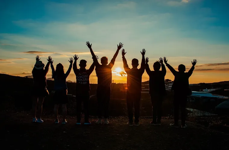 Silhouetten einer Gruppe junger Menschen mit erhobenen Armen im Sonnenuntergang