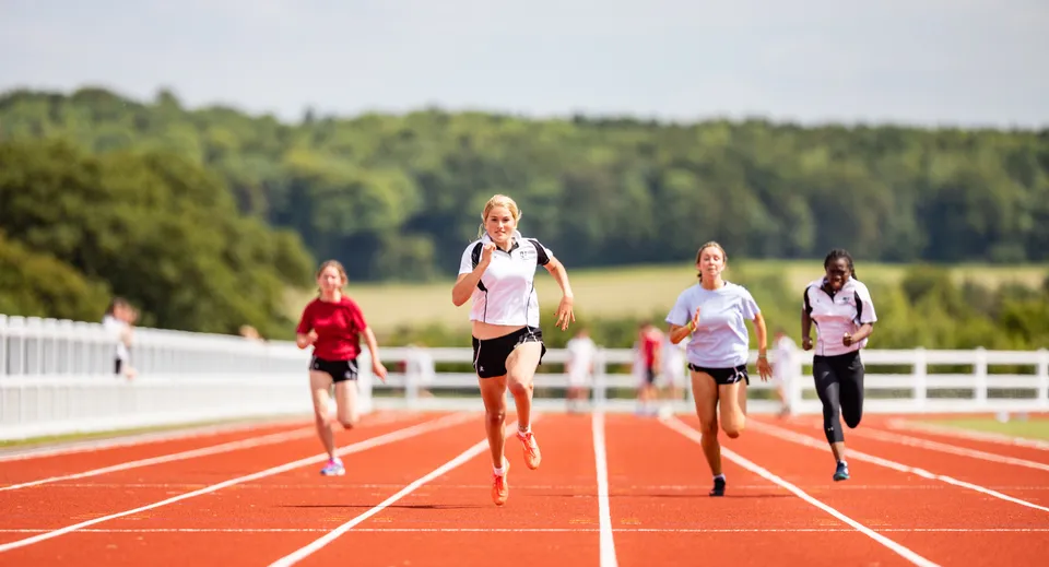 Un gruppo di runner scatta sulla pista di atletica rossa nel campus della Dauntsey’s School davanti a un paesaggio boscoso.