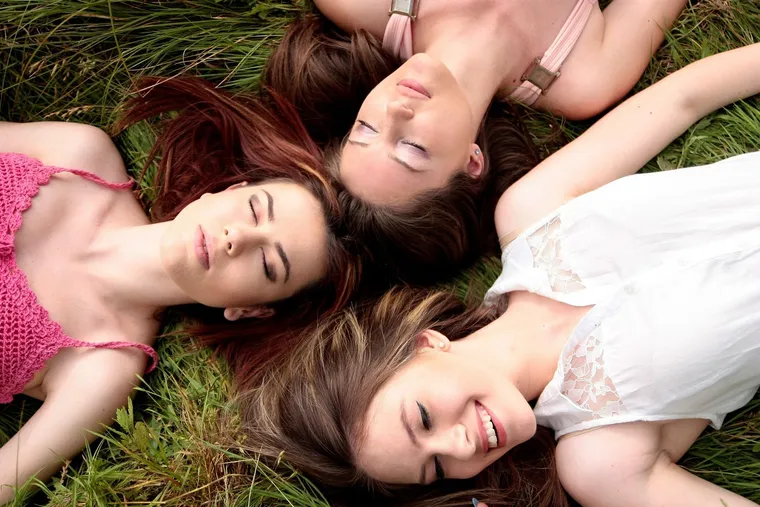 Drei junge Frauen liegen mit geschlossenen Augen lächelnd im Gras