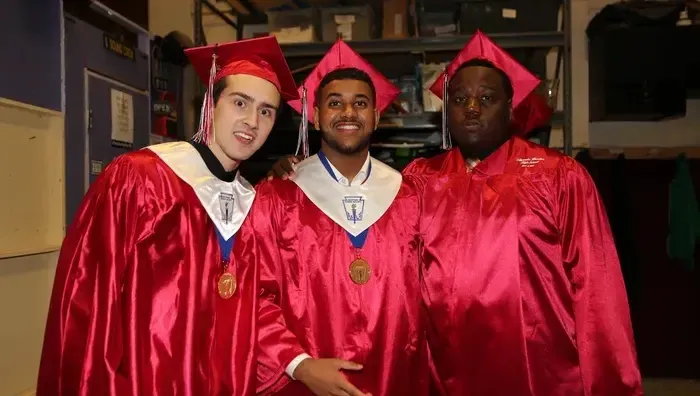 Tres graduados con togas rojas están juntos en el pasillo de la Hamilton Boy's High School.