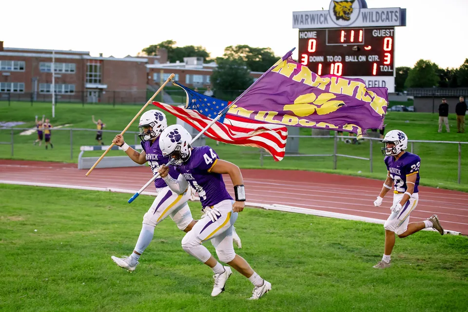 Un gruppo di giocatori di football della Warwick Valley High School porta bandiere e stendardi della propria squadra e del proprio paese sul campo di gioco.