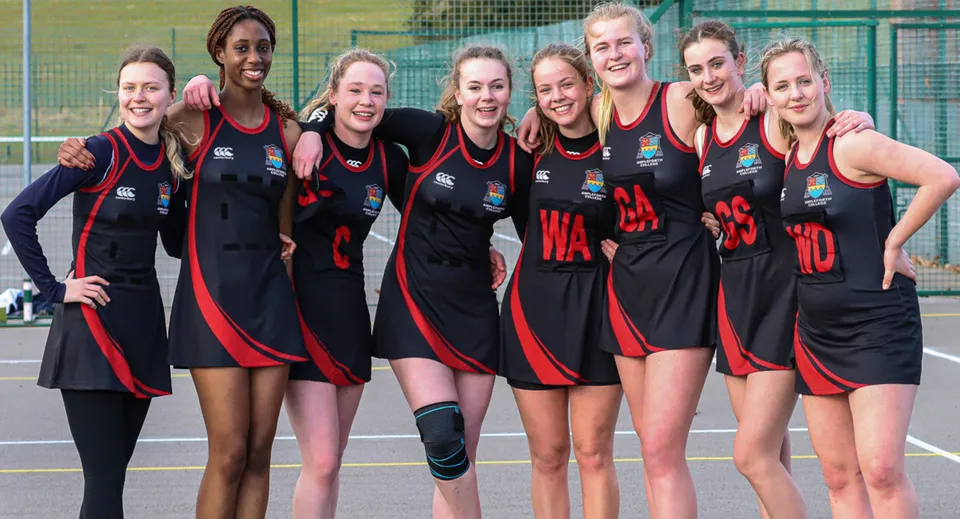 Un gruppo di atlete posa insieme sul campo sportivo dell'Ampleforth College davanti a una recinzione.