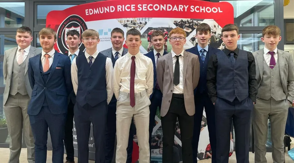 Un gruppo di studenti in abito formale si trova davanti a un cartello della Edmund Rice Secondary School.