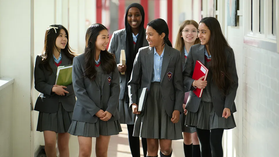 Studentesse e studenti della Townley Grammar School camminano insieme lungo un corridoio con pareti rosse.