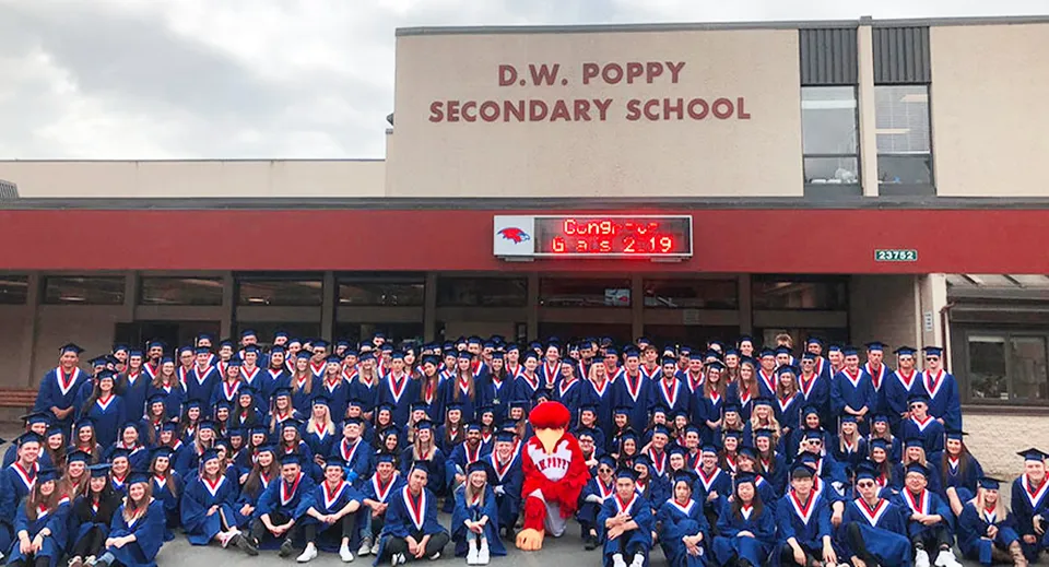 Un gruppo di studenti e studentesse davanti all'edificio della D.W. Poppy Secondary School.