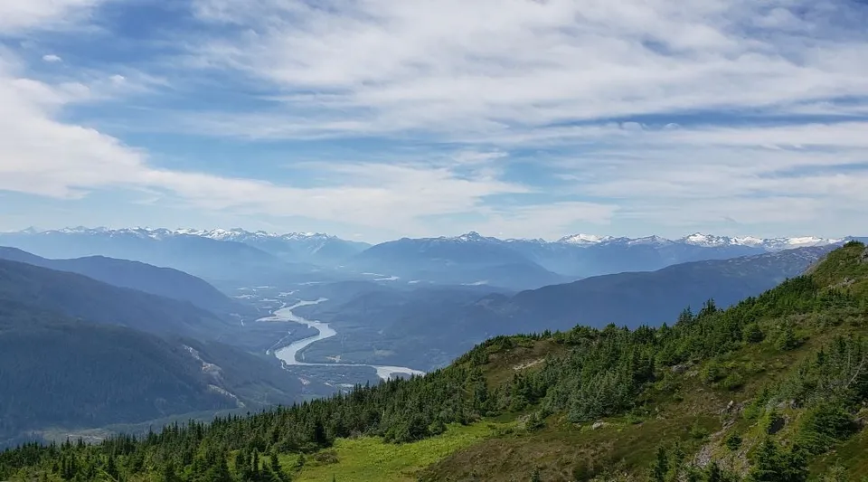 Un paesaggio montano verde con un fiume e cime innevate sullo sfondo vicino alla Caledonia Secondary School.