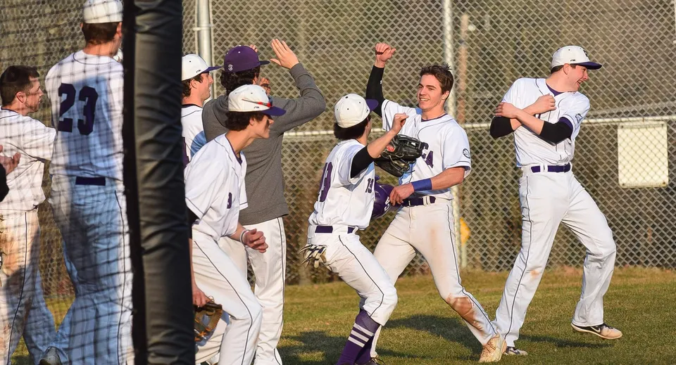Un gruppo di giocatori di baseball della Cushing Academy festeggia sul campo da baseball accanto a una recinzione.
