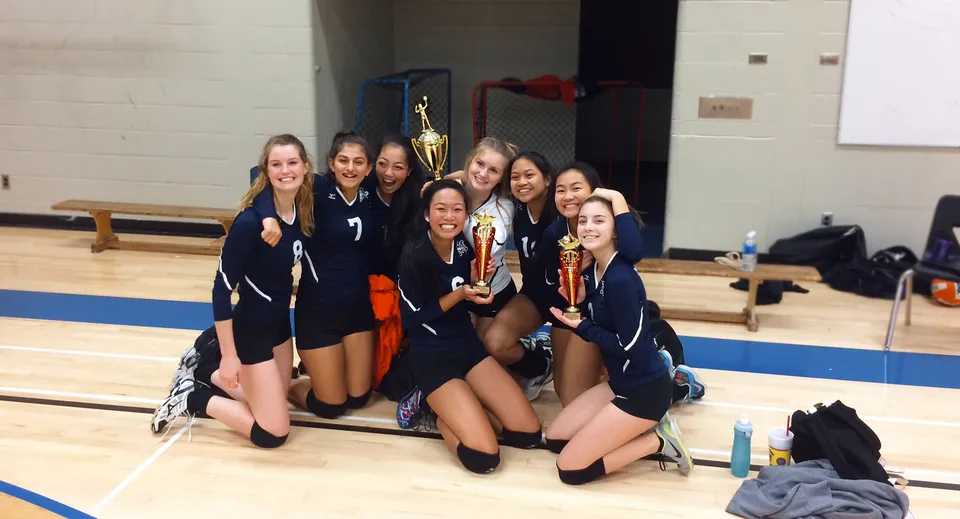 Studentesse della Matthew McNair Secondary School festeggiano la loro vittoria nella palestra con trofei in mano.