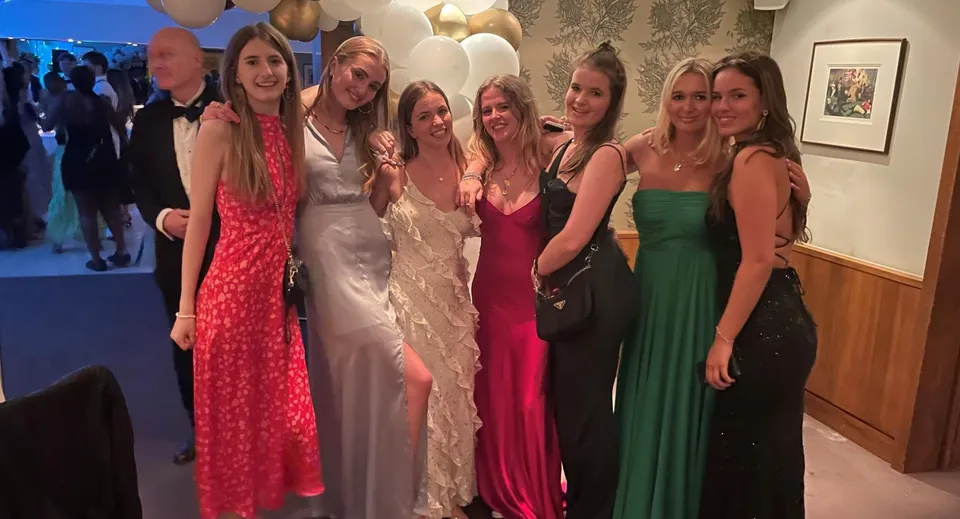 Un gruppo di studentesse della Heathfield School a Ascot posa vestito a festa durante una celebrazione con palloncini sullo sfondo.