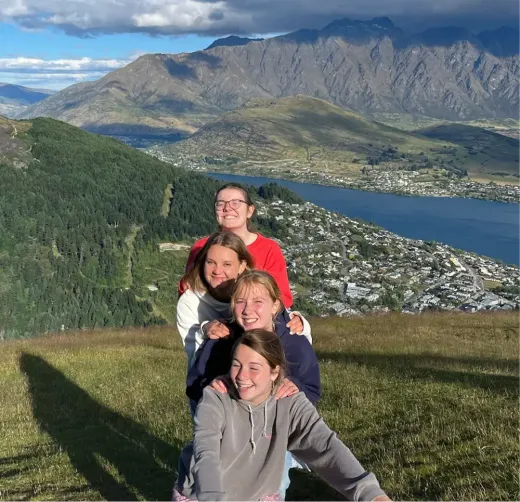 Vier Mädchen posieren auf einem Hügel mit Blick auf See und Berge in Neuseeland