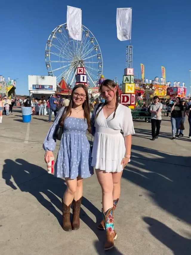 Due studentesse in stivali da cowboy sorridono davanti alla ruota panoramica di una fiera statunitense