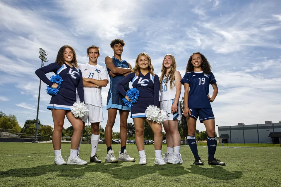 Un gruppo di cheerleader della Linfield Christian School si trova insieme su un campo erboso sotto un cielo nuvoloso.