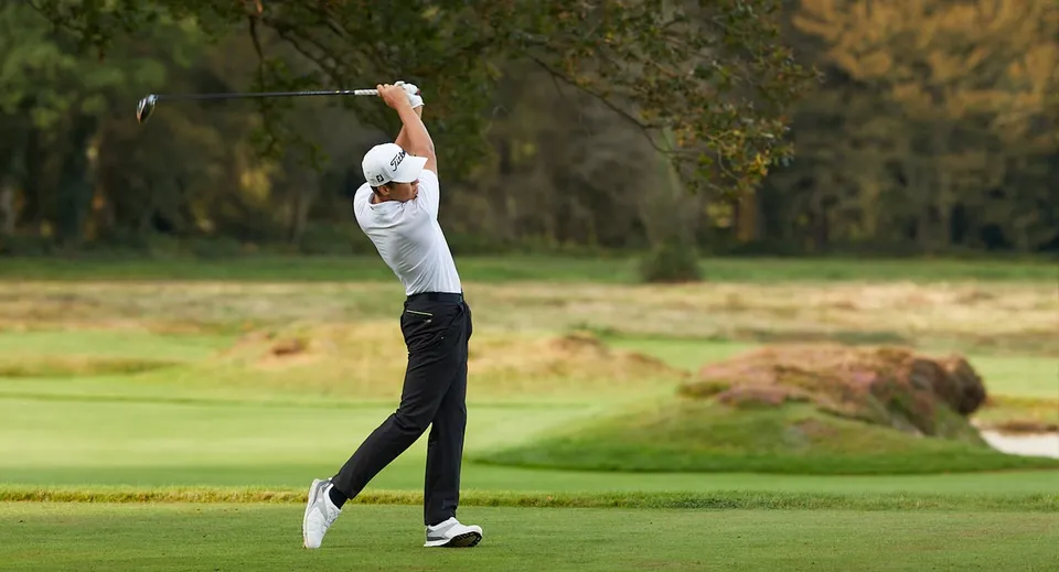 Un giocatore di golf in maglia bianca fa uno swing con una mazza sul campo da golf dell'Epsom College.