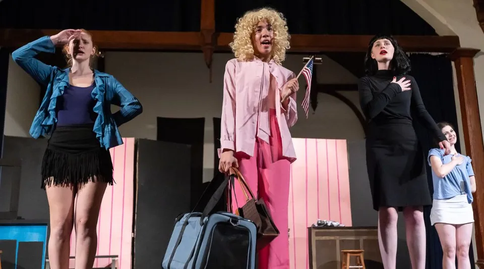 Un gruppo di donne in costumi colorati si trova sul palco della Miller School of Albemarle davanti a uno sfondo architettonico.