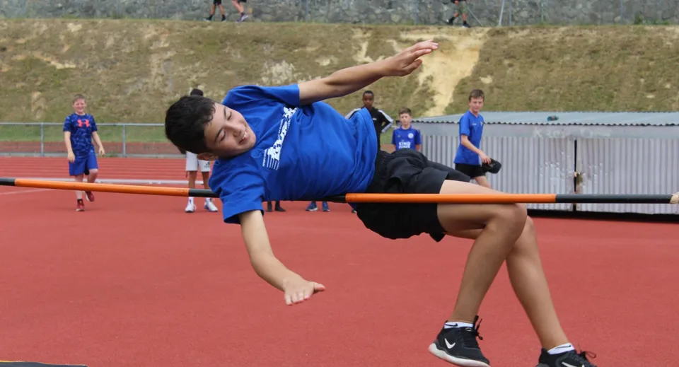 Uno studente del Rongotai College esegue un esercizio di ginnastica su una superficie rossa, mentre altre persone sono visibili sullo sfondo.