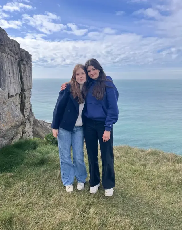 Due amiche abbracciate su una scogliera erbosa affacciata sul mare