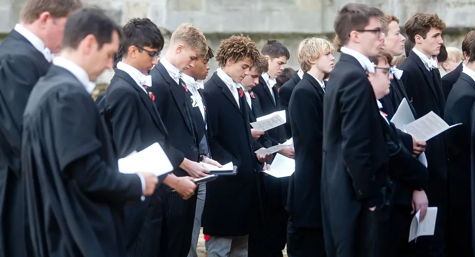 Un gruppo di studenti dell'Eton College in abito formale è in piedi davanti a un edificio in pietra con dei documenti in mano.