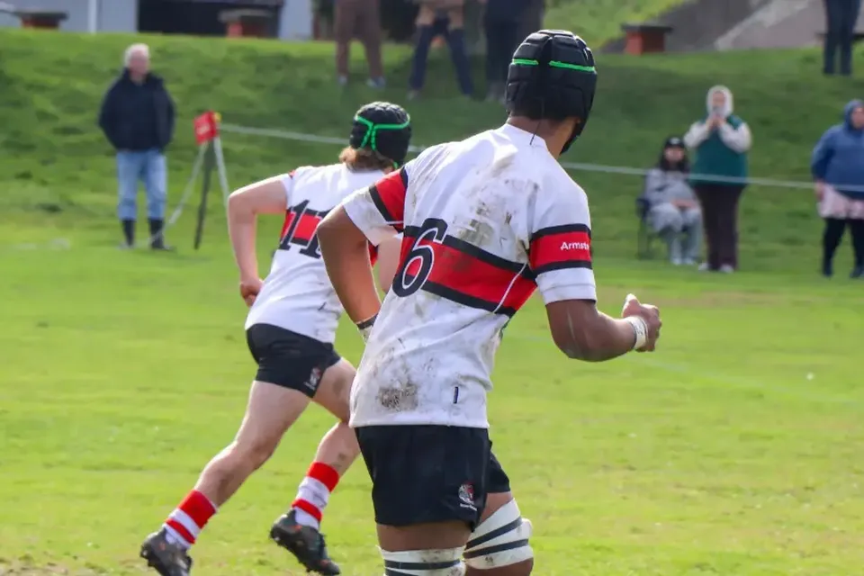 Due giocatori di rugby di The Scots College corrono sul campo erboso con il casco protettivo durante una partita.