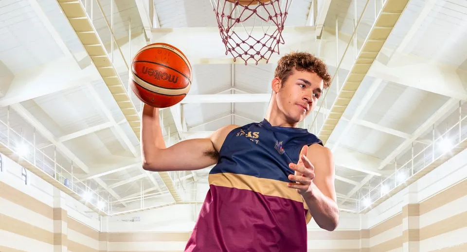 Uno studente della Toowoomba Anglican School tiene in mano un pallone da basket davanti al canestro sul campo da gioco.