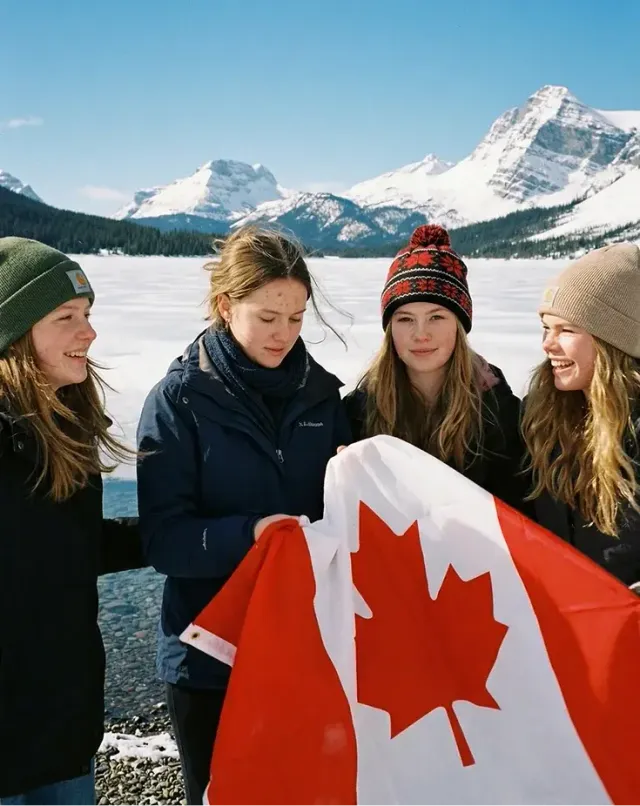 Quattro studentesse con berretti invernali reggono la bandiera canadese davanti a montagne innevate