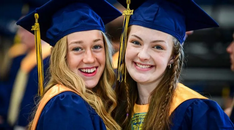 Due studentesse della Notre Dame High School a Calgary posano insieme alla cerimonia di diploma in toghe e tocchi blu.