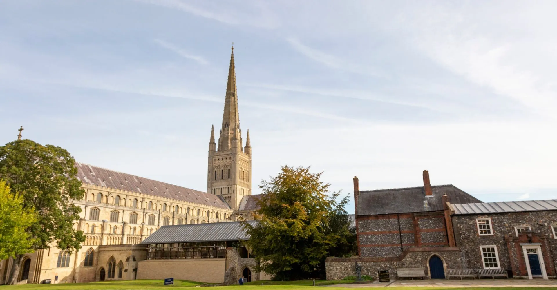 L'alta torre di una cattedrale svetta sui fabbricati all'interno del campus della Norwich School sotto un cielo nuvoloso.