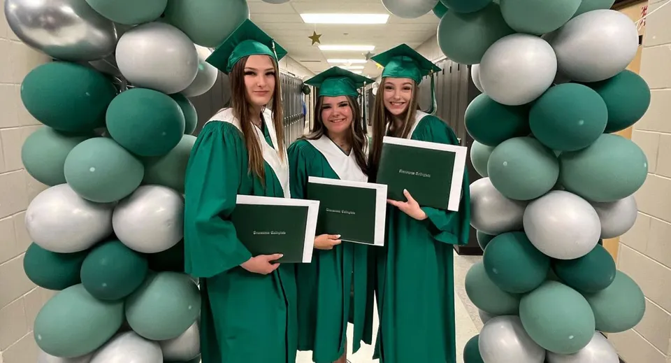 Un gruppo di giovani donne in toga e tocco da diploma verdi durante la foto ricordo nel campus della Transcona Collegiate.