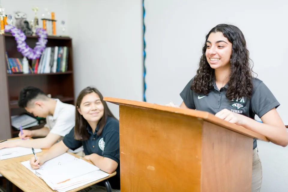 Tre studentesse della Fairmont Prep Academy sono in classe: una è al podio e due sono sedute ai banchi.
