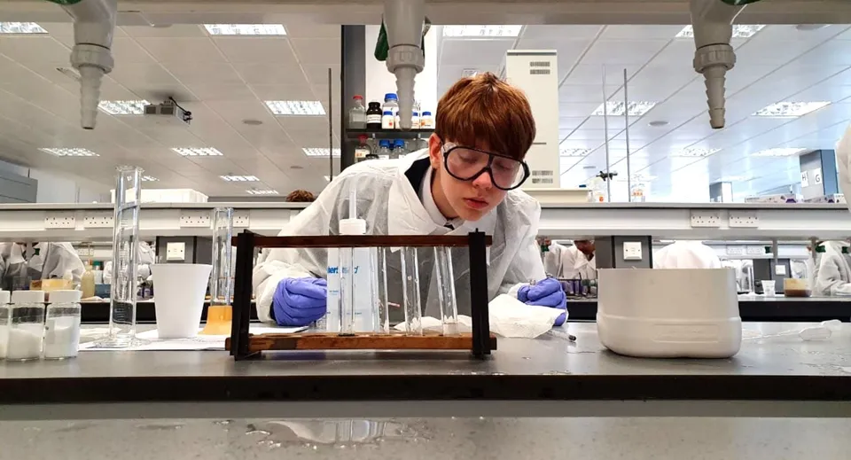 Una persona in abbigliamento protettivo esegue un esperimento nel laboratorio della Strathallan School.