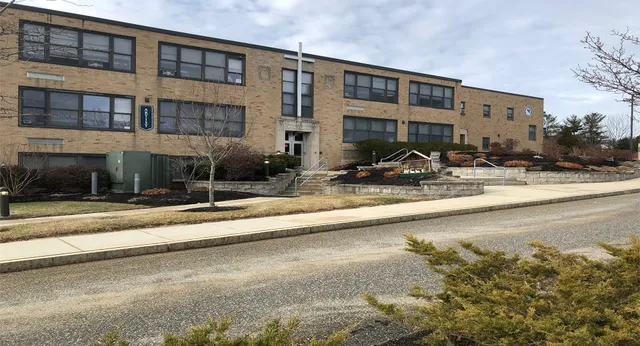 L'edificio in mattoni a più piani della St. Thomas Aquinas High School con ampie finestre lungo una strada alberata.