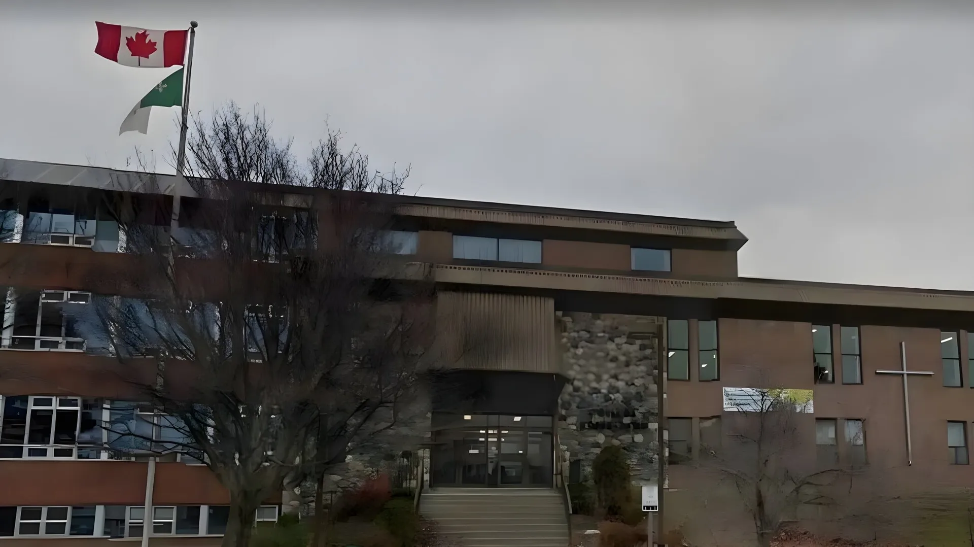 L'edificio a più piani del Collège Notre-Dame con la bandiera canadese e palestinese sul tetto contro un cielo nuvoloso.