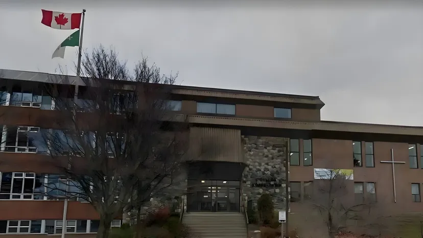 L'edificio a più piani del Collège Notre-Dame con la bandiera canadese e palestinese sul tetto contro un cielo nuvoloso.