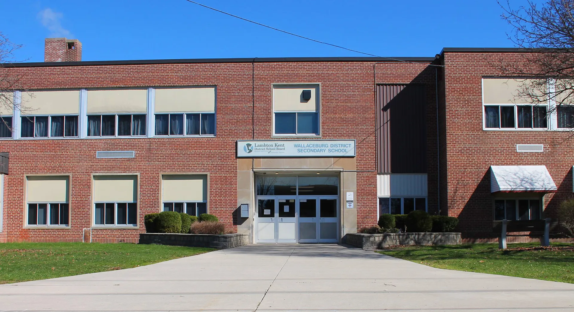 L'edificio in mattoni a due piani della Wallaceburg District High School con grandi finestre si erge sotto un cielo azzurro e limpido.