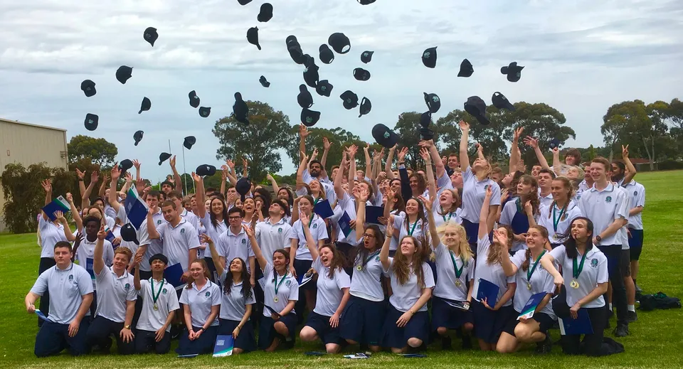 Un gruppo di studenti della Modbury High School lancia i propri cappelli in aria all'aperto per festeggiare.