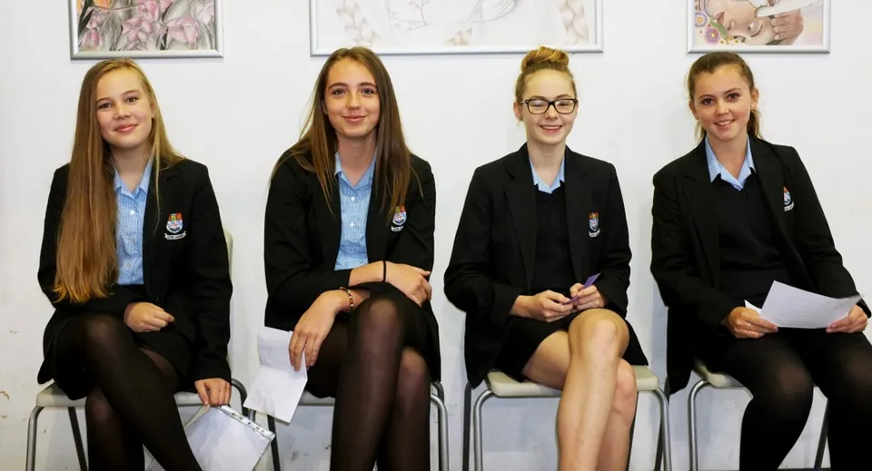 Quattro studentesse della Truro High School for Girls sono sedute in classe davanti a opere d'arte incorniciate sulla parete.