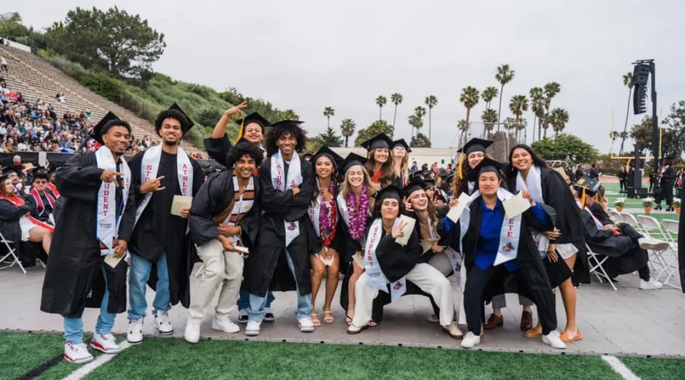 Un gruppo di laureati e laureate del Santa Barbara City College posa all'aperto davanti ad alberi e un prato.