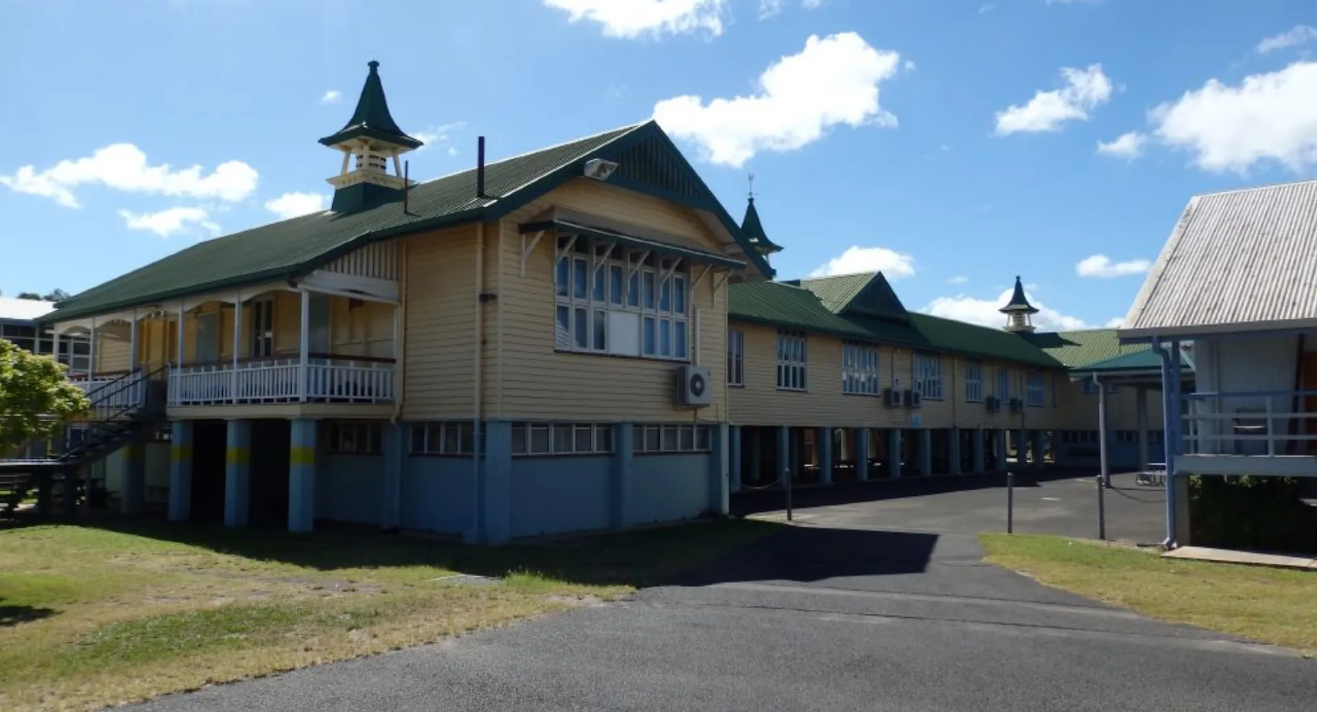 L'edificio in legno a più piani della Bundaberg State High School si trova circondato da un prato sotto un cielo blu con nuvole bianche.