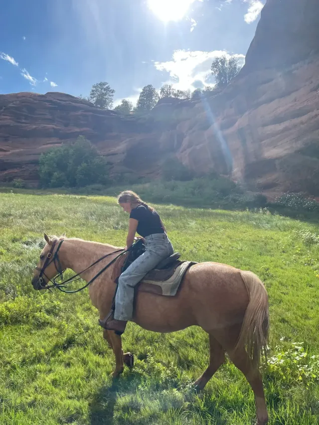Studentessa a cavallo in un prato ai piedi di formazioni rocciose rosse negli Stati Uniti