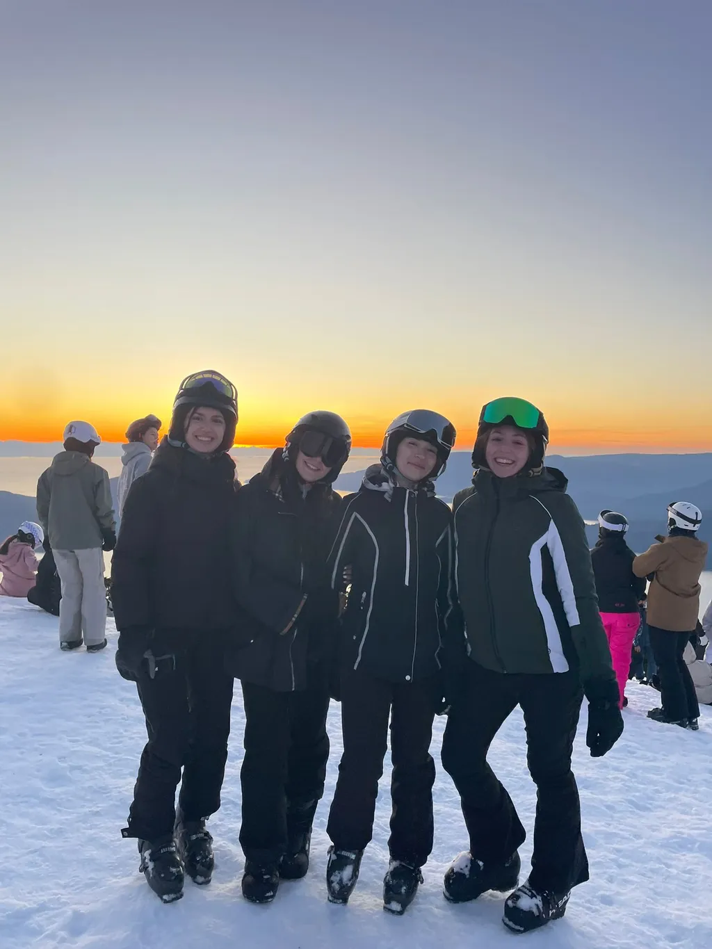 Quattro studentesse in tenuta da sci sorridono al tramonto in cima a una pista innevata in Canada