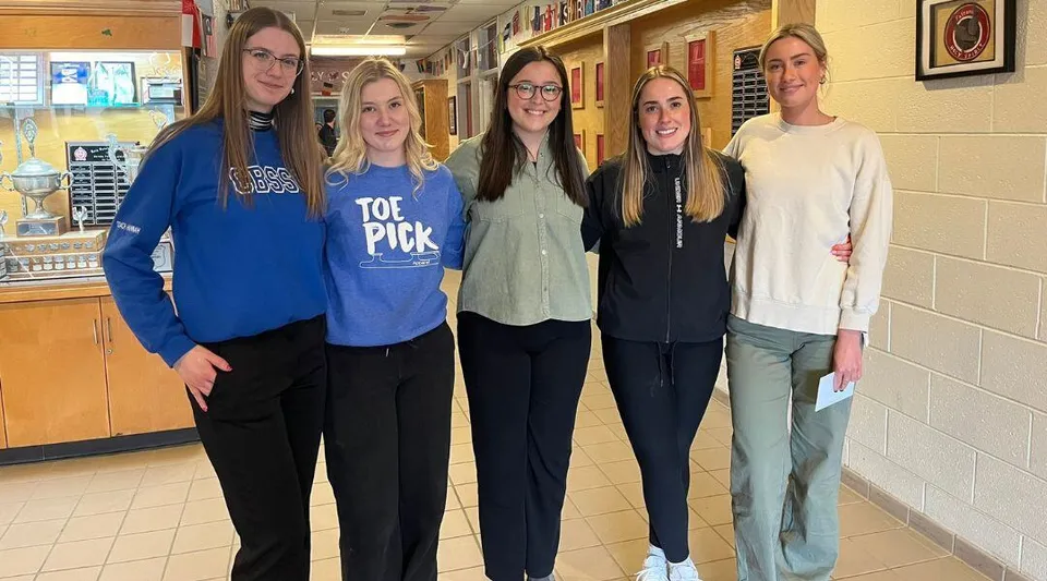 Cinque studentesse sono insieme nel corridoio della Holy Spirit High School con armadietti sullo sfondo.