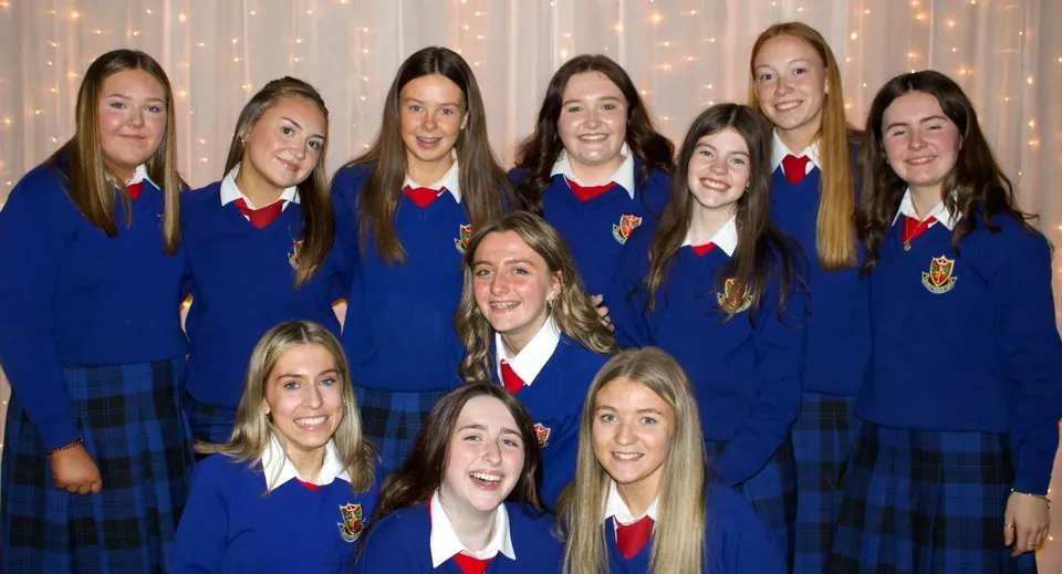 Un gruppo di studentesse in divisa blu con dettagli rossi posa davanti a uno sfondo scintillante nel campus della St. Vincent's Secondary School.