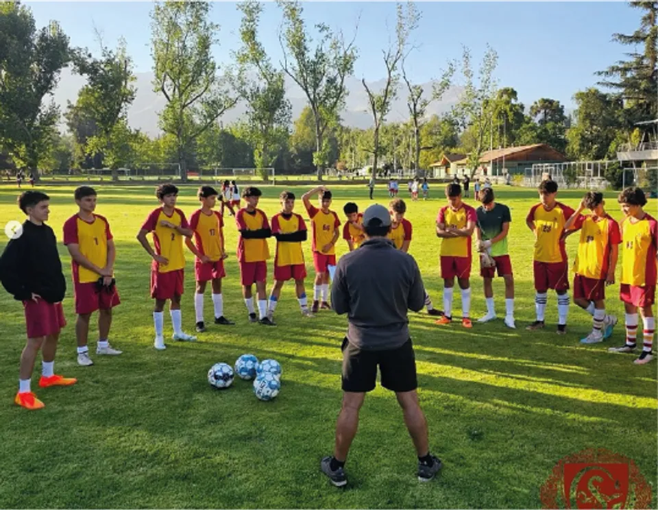 Studenti del Colegio San Gabriel si trovano sul campo sportivo durante un allenamento di calcio sotto la guida di un allenatore.