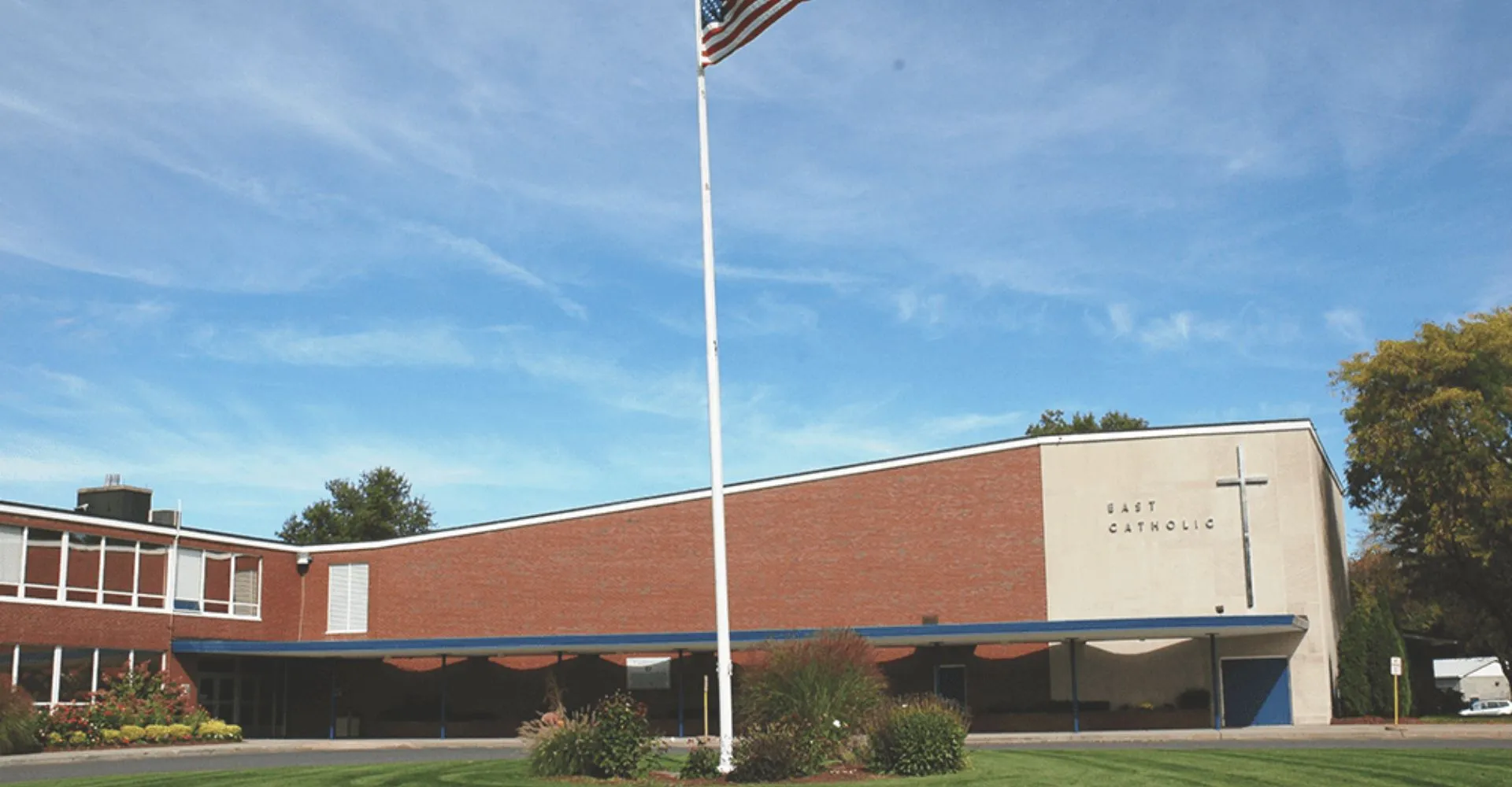L'edificio in mattoni della East Catholic High School con una grande bandiera americana contro il cielo blu.