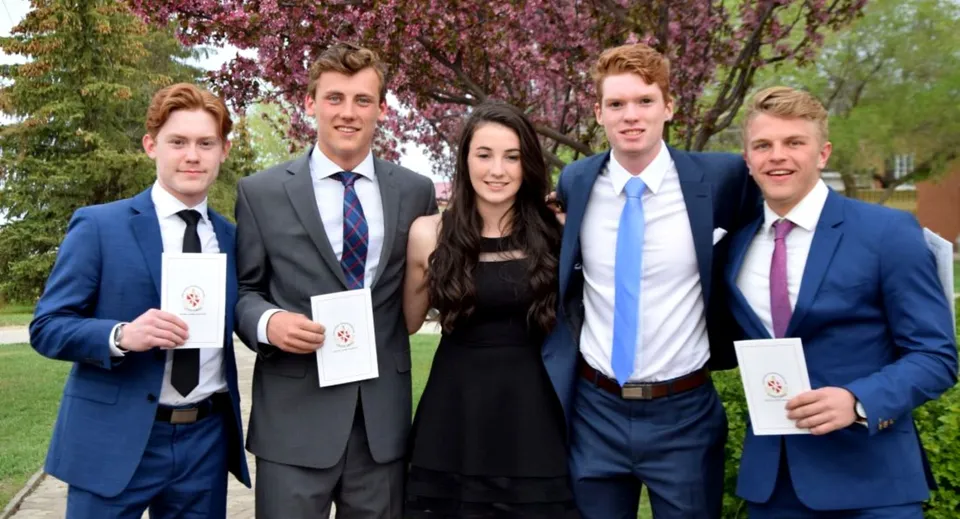 Un gruppo di cinque giovani adulti è in piedi nel parco del campus dell'Athol Murray College of Notre Dame con alberi in fiore sullo sfondo.