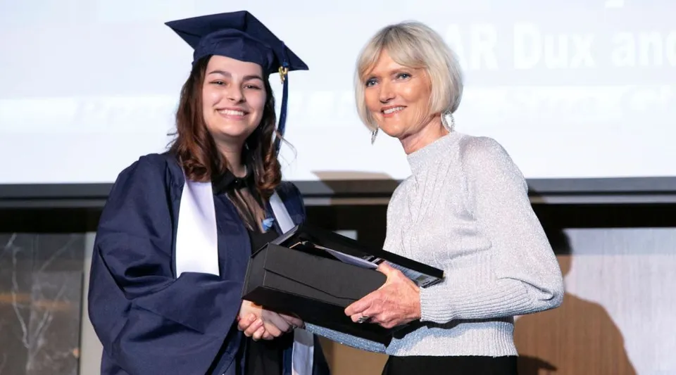 Una giovane donna in toga sta insieme a una donna più anziana e tiene in mano un diploma sul campus della Morley Senior High School.