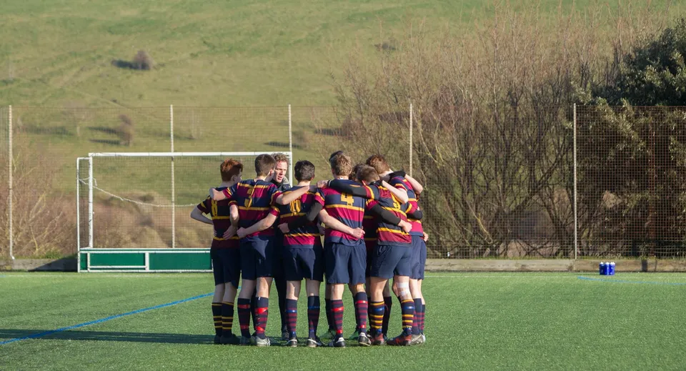 Un gruppo di studenti si trova sul campo sportivo del Brighton College circondato da un paesaggio verde.